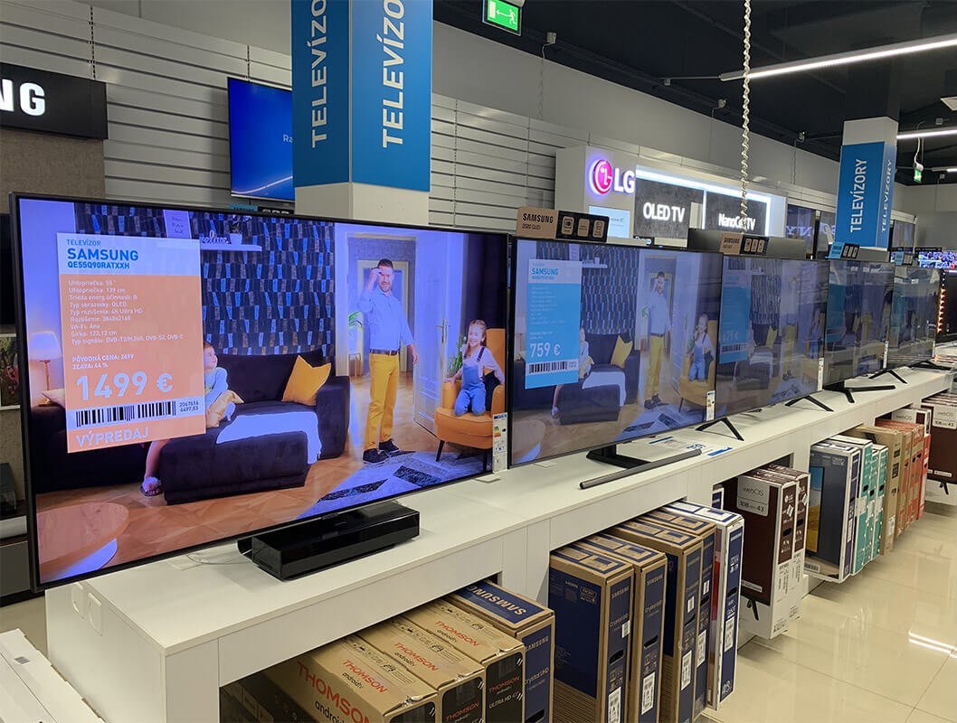 Exigo v predajni: televízor s produktovým videom a cenovkou vykreslenou na obrazovke